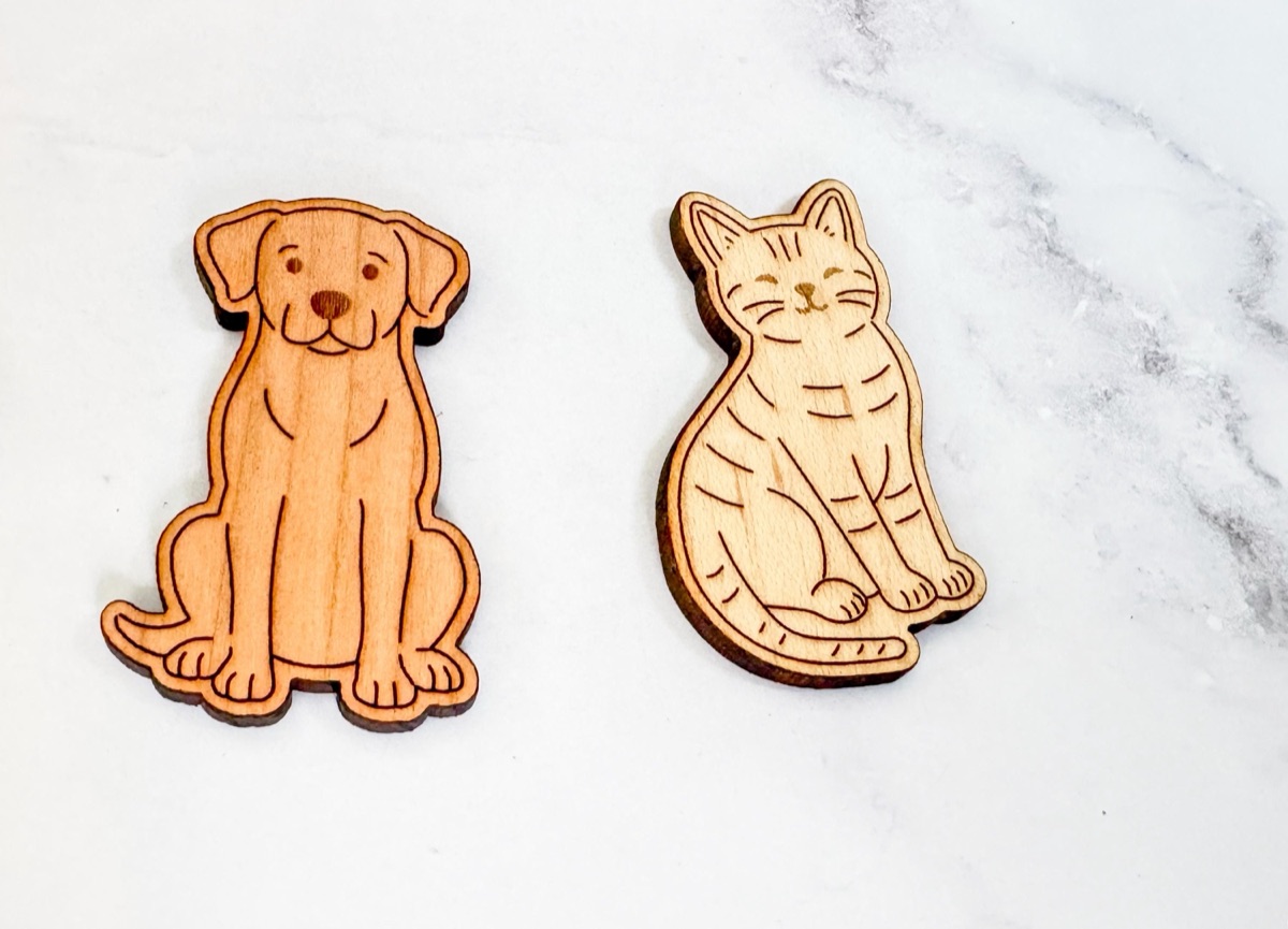 Detail of a solid cherry dog and a solid maple cat playing token, laser-engraved with facial features, tabby stripes, and toe lines, showing the color contrast between the two hardwoods