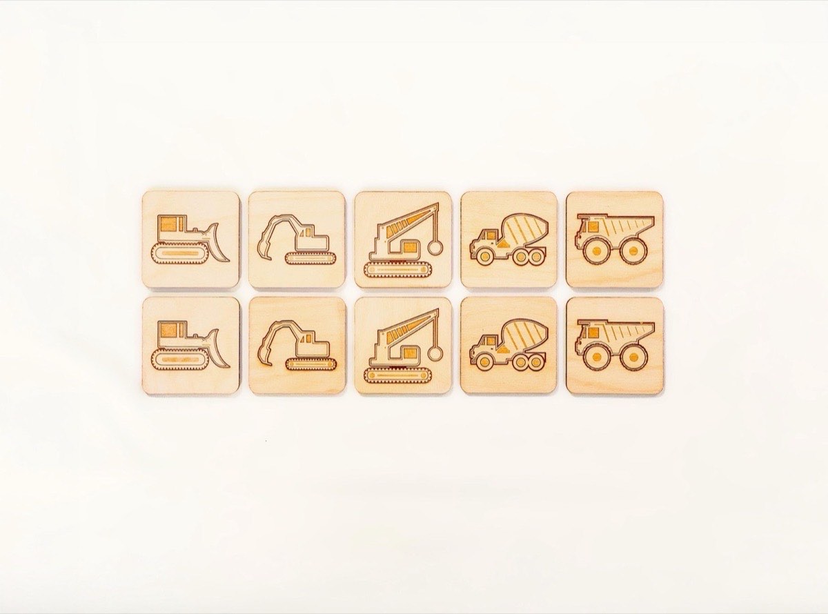 10-piece neutral-colored construction vehicle memory match set on white, featuring five matching pairs of laser-engraved bulldozer, excavator, crane, cement mixer, and dump truck designs on neutral Baltic birch tiles.  On a flat white background
