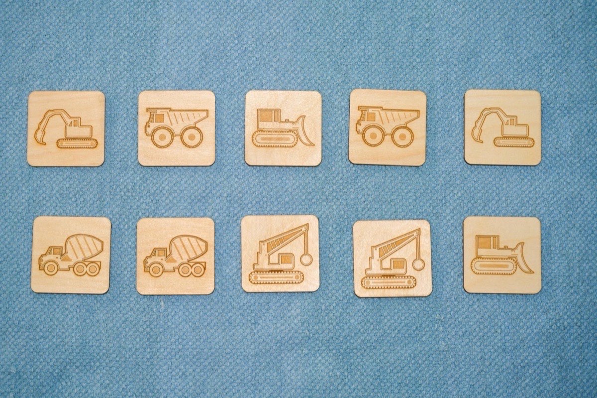 10-piece neutral-colored construction vehicle memory match set on a blue Montessori floor mat, arranged as five matching pairs: cement mixer, dump truck, wrecking ball crane, bulldozer, and excavator in neutral Baltic birch