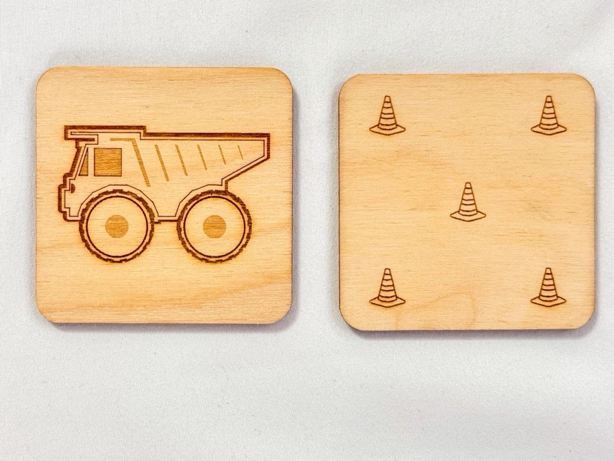 Front and back views of a single memory match tile, showing the laser-engraved dump truck on one side and the five traffic cone pattern on the reverse, demonstrating the neutral Baltic birch construction.  Rounded edges.  The product is on a white fabric background