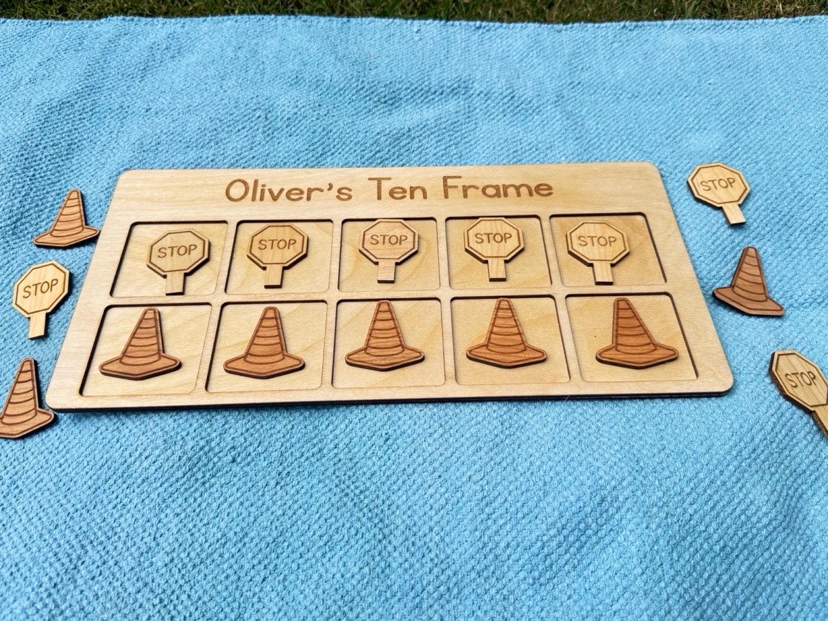 Construction-themed ten frame on a blue blanket in grass, five stop sign counters above five traffic cone counters with extra pieces scattered around for outdoor counting play