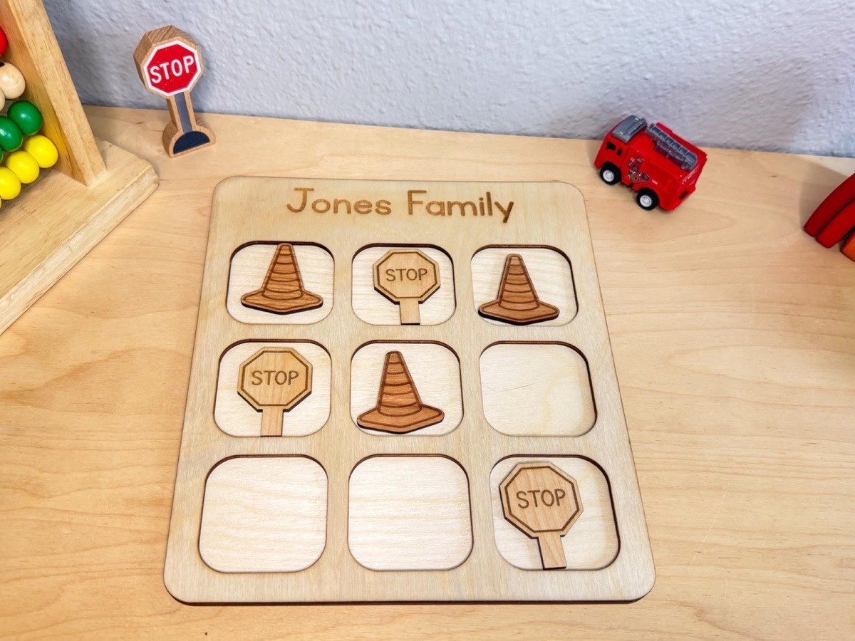 Construction tic tac toe on a playroom desk with a red toy fire truck and wooden stop sign nearby, six laser-engraved cone and stop sign pieces mid-game on the board