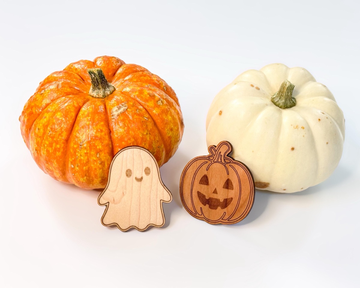 A maple ghost counter and a cherry jack-o'-lantern counter standing upright in front of a small orange pumpkin and a small white pumpkin on a white tabletop