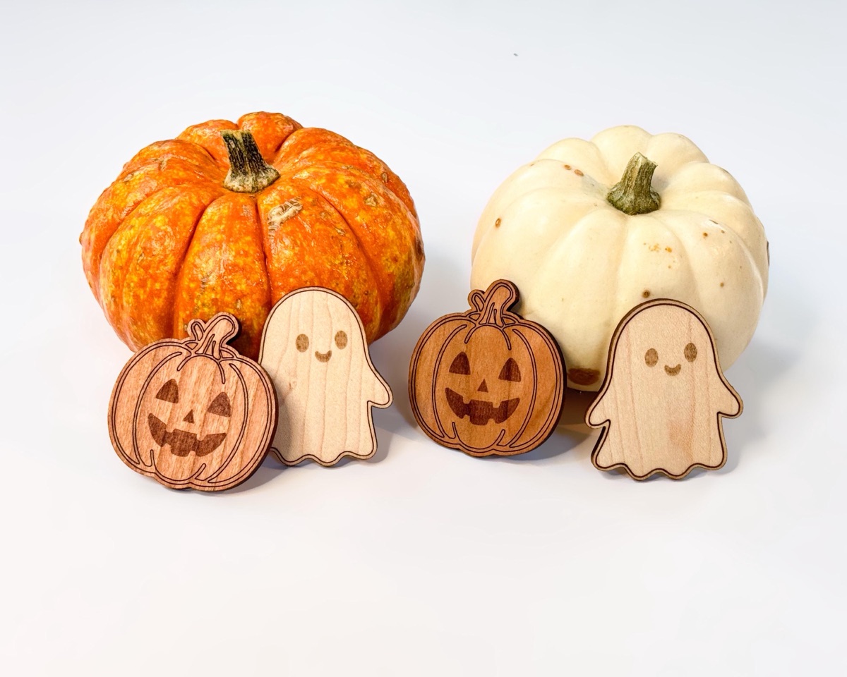 Two cherry jack-o'-lantern counters and two maple ghost counters lined up in alternating order in front of an orange pumpkin and a white pumpkin on a white tabletop