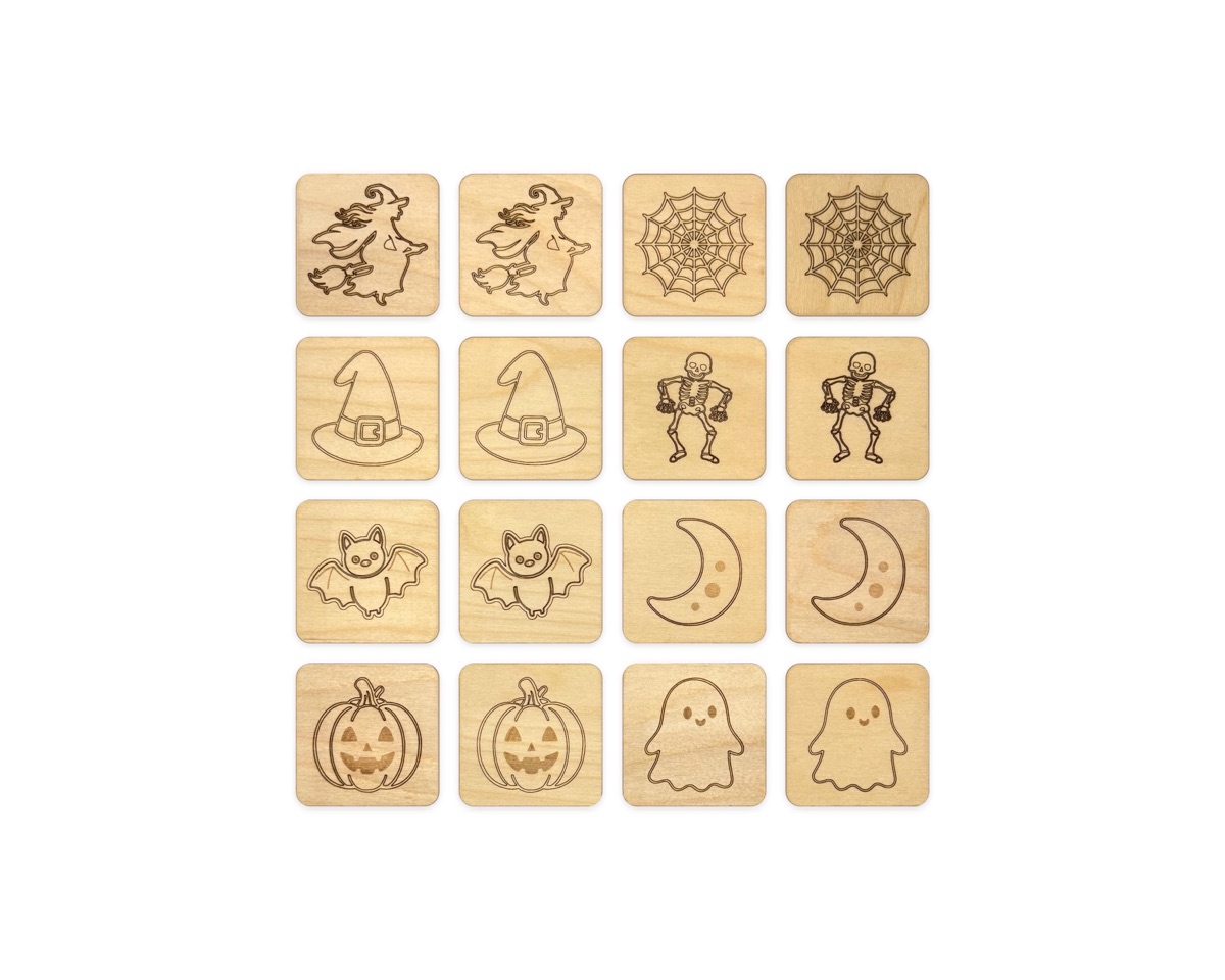 Sixteen wooden memory match tiles in a four by four grid of eight pairs: a witch on a broom, a spider web, a witch hat, a skeleton, a bat, a crescent moon, a jack-o'-lantern, and a ghost, engraved on Baltic birch with rounded corners
