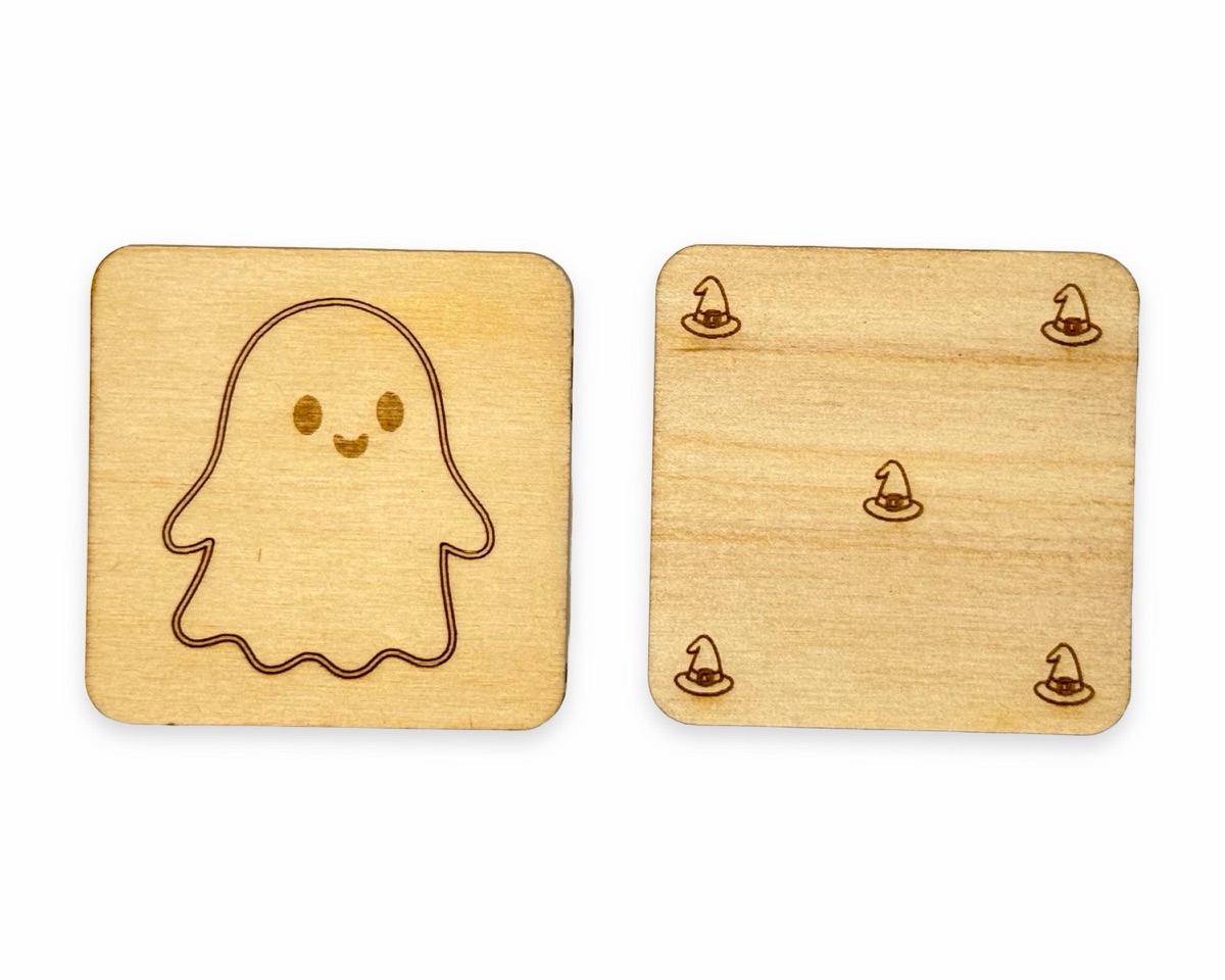 One tile front and one tile back side by side: a smiling ghost outline engraved on the front, and five small witch hats engraved in the corners and center of the back, on square Baltic birch with rounded corners