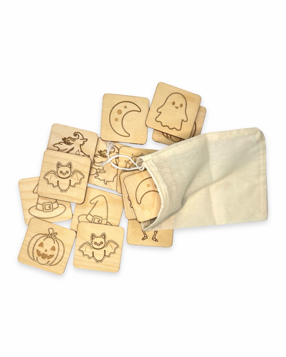 Natural cotton drawstring bag lying open with Halloween memory tiles spilling out, including the crescent moon, ghost, bat, witch on a broom, witch hat, and jack-o'-lantern designs