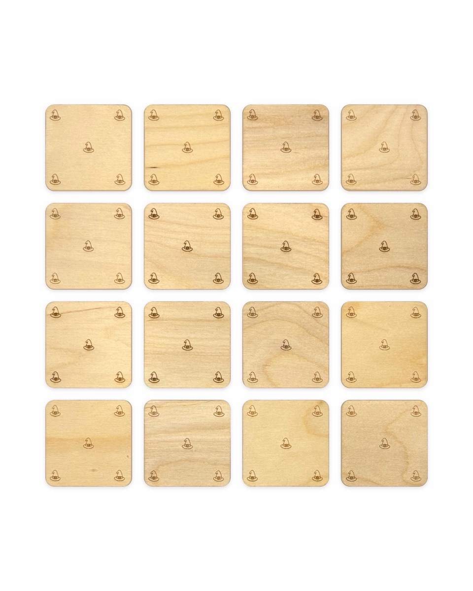 Reverse sides of all sixteen memory match tiles in a four by four grid, each engraved with five small witch hats in the corners and center, showing the light grain of the Baltic birch