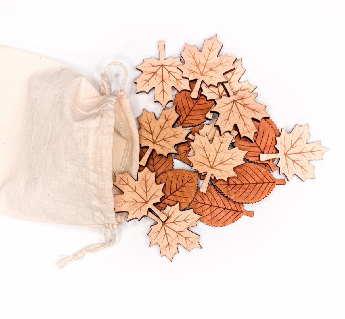 Wooden leaf counters in pale maple and warm cherry spilling from a cotton drawstring bag