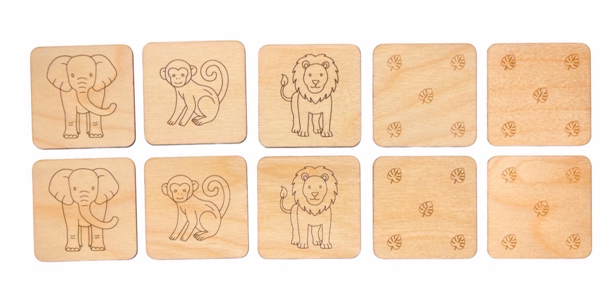 Ten wooden safari animal memory match tiles in two rows, with elephant, monkey, and lion faces showing on three pairs and the reverse leaf-pattern side showing on the remaining two pairs