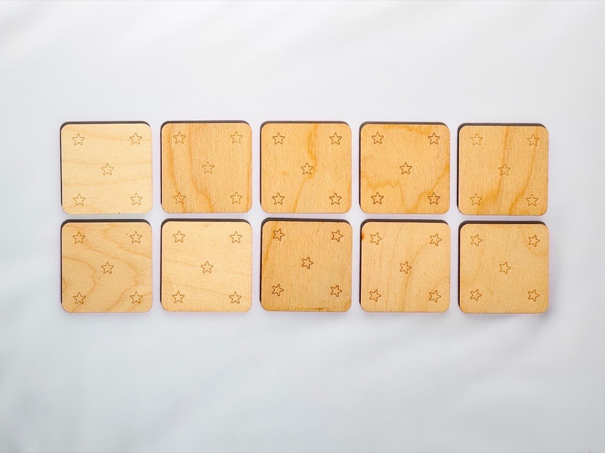 Backs of ten neutral-colored wooden memory match tiles, each engraved with five-star constellation pattern in corners and center of Baltic birch squares