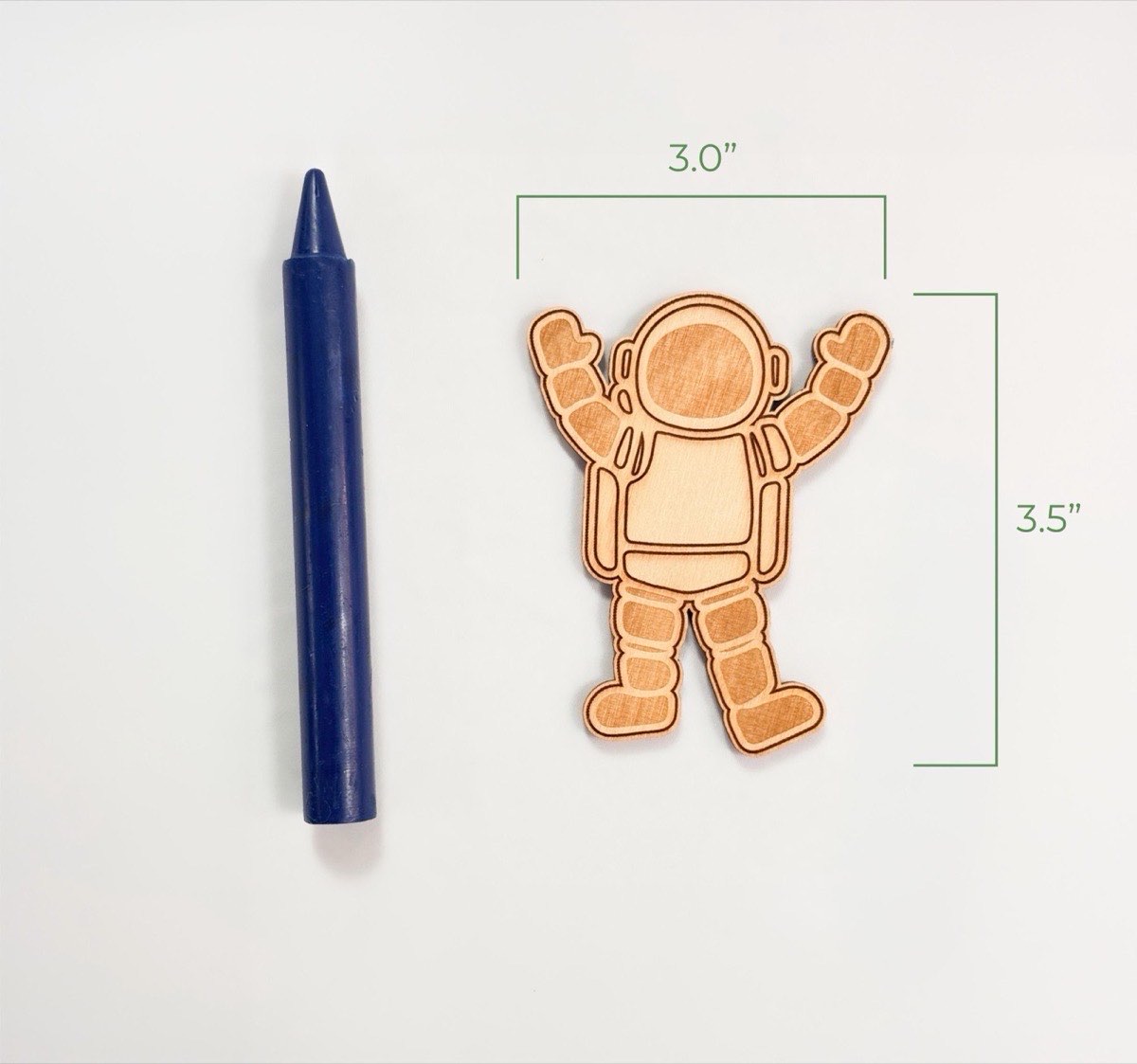 Size reference photo of the wooden astronaut piece, 3 inches wide and 3.5 inches tall, next to a jumbo crayon